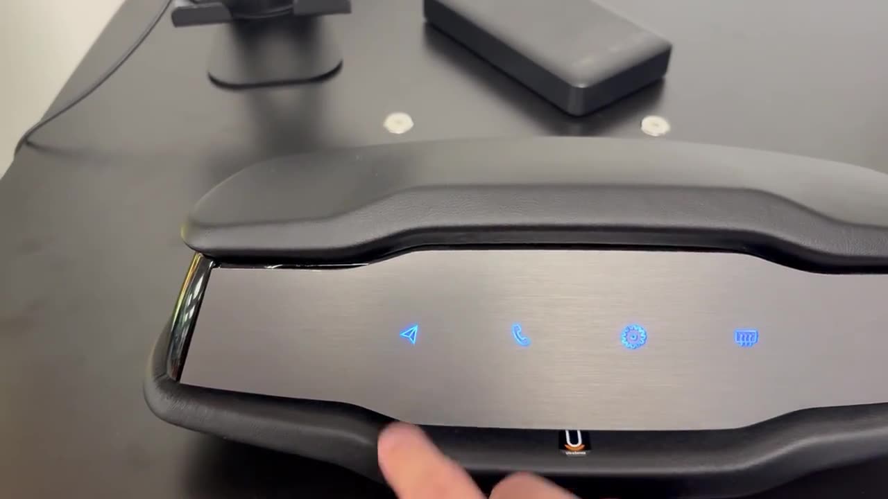 A finger pressing icons along a dark metal centre-console bar, each one lighting blue through the unbroken metal as it is touched.