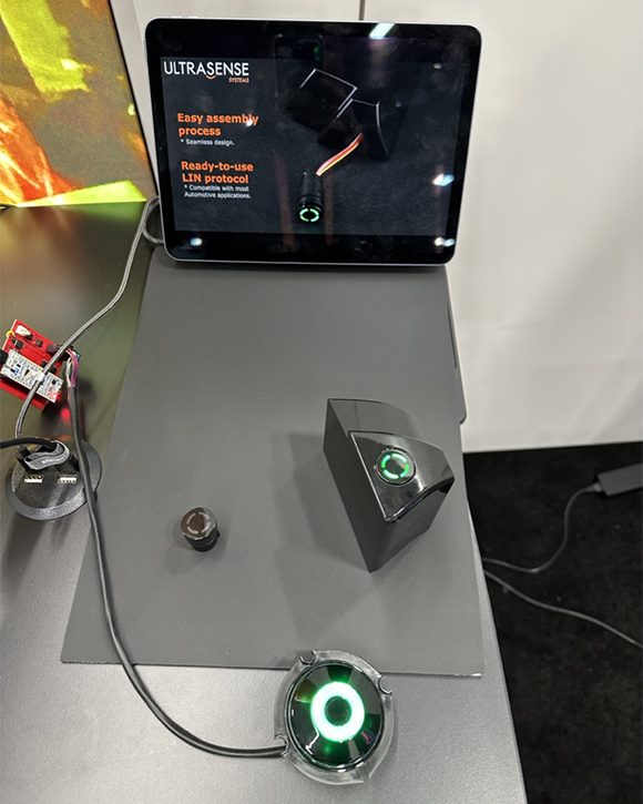 A bench demonstration rig on a grey worktop -- a tablet on a stand, a wired test fixture, and a round sensor puck lit green.