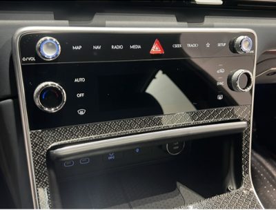 A production car centre console, its climate and media controls lit through a solid patterned fascia, with rotary dials at each end.