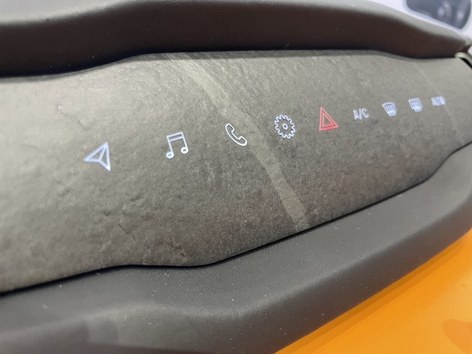 A car console surface in mottled grey stone with six lit white control icons showing through the stone itself.