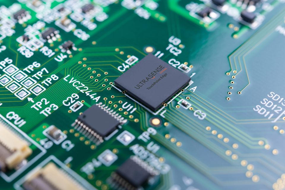 Macro close-up of a green printed circuit board with an integrated circuit and gold signal traces running away from it.